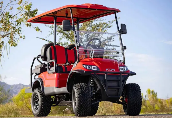 Red ICON i40L lifted golf cart with off-road tires and black-red seating parked on rugged Florida terrain